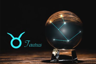Taurus Zodyak burcunun yanındaki takımyıldızlı kristal küre, siyah üzerine izole edilmiş ahşap masa.