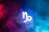 blau beleuchtetes Tierkreiszeichen Steinbock mit buntem Rauch auf Hintergrund