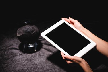 Siyah kadife kumaş üzerinde kristal kürenin yanında dijital tablet tutan astrolog görüntüsü.