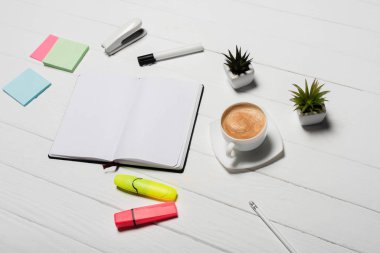 Ofis malzemeleri, bitkiler ve kahvenin bulunduğu beyaz ahşap işyeri