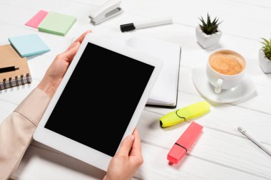 İş yerinde elinde dijital tabletle ofis malzemeleri ve kahve taşıyan bir kadın görüntüsü.