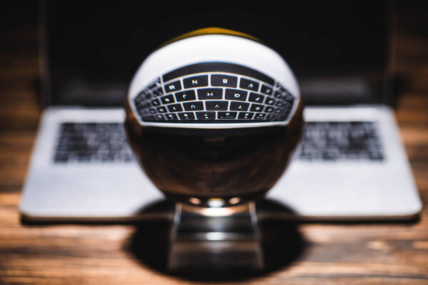 selective focus of crystal ball near laptop on wooden table on black background