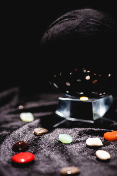 close up view of crystal ball with fortune telling stones on black velvet cloth