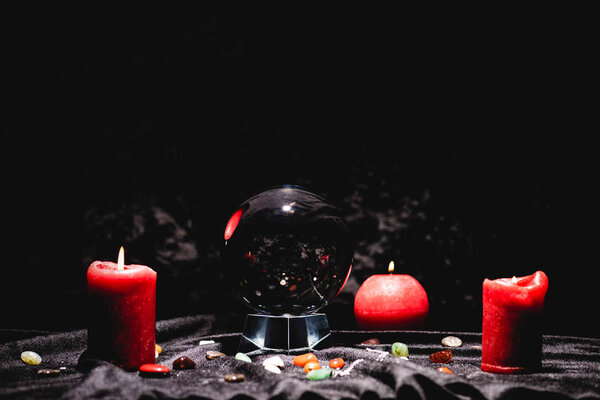 хрустальный шар с камнями судьбы и свечами на черной бархатной ткани
