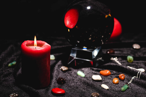 selective focus of crystal ball with fortune telling stones and candle on black velvet cloth