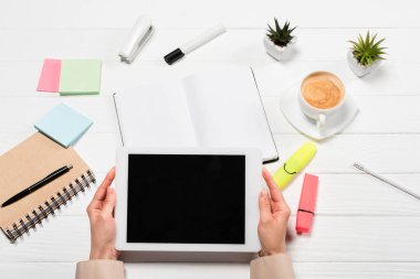 İş yerinde elinde dijital tabletle ofis malzemeleri ve kahve taşıyan bir kadın görüntüsü.