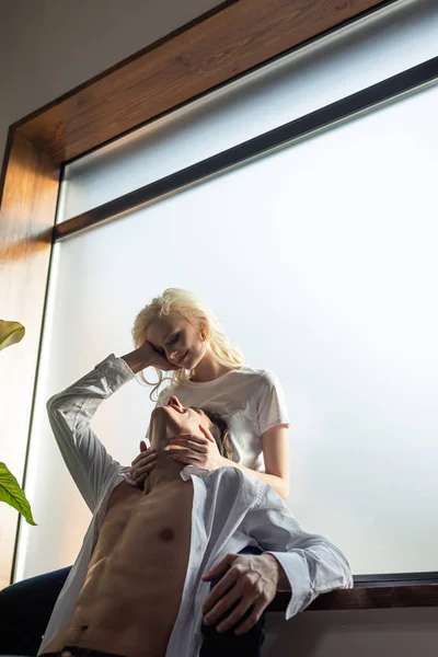 Smiling Woman Embracing Shirtless Boyfriend While Sitting Windowsill — Stock Photo, Image
