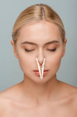 naked young woman with wooden pin on nose and closed eyes isolated on grey  clipart