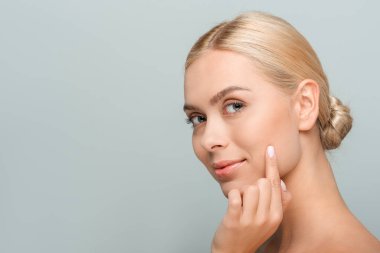 Genç ve güzel bir kadın kameraya bakıyor ve gri renkte izole edilmiş yüzlere dokunuyor. 