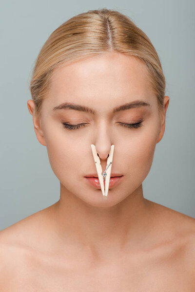 naked young woman with wooden pin on nose and closed eyes isolated on grey 