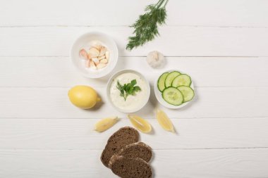 Tzatziki sosunun beyaz ahşap arka plandaki malzemelerle üst görüntüsü