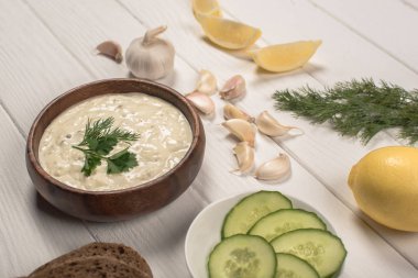 Traditional Greek tzatziki sauce with fresh ingredients on white wooden background clipart
