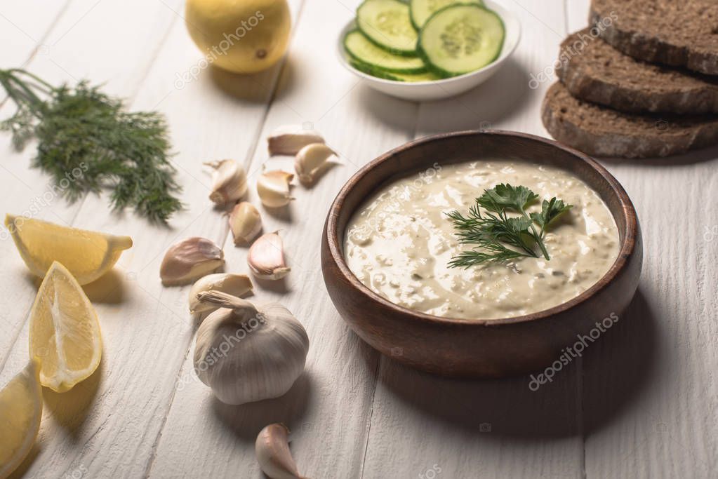 Tzatziki sauce in wooden bowl with ingredients on white wooden background