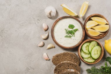 Tzatziki sosunun üst görüntüsü, taş zeminde ekmek ve organik malzemeler var.