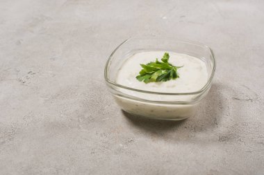Tasty homemade tzatziki sauce with greenery on stone surface clipart