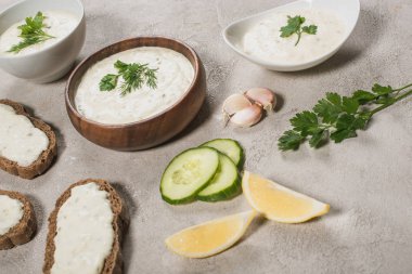 Homemade tzatziki sauce in bowls with fresh ingredients on stone surface clipart