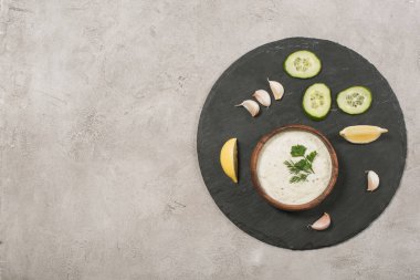 Taş zemin üzerinde sebze ve limon dilimleri olan tzatziki sosunun üst görüntüsü