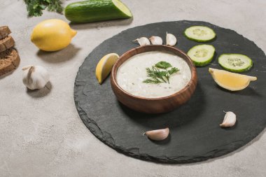 Gourmet tzatziki sauce with raw ingredients on stone surface clipart