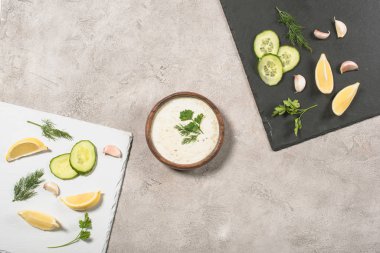 Tzatziki sosunun üst görüntüsü ve taş zeminde taze malzemeler.