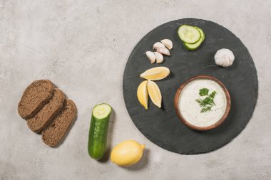 Tzatziki sosunun en üst görüntüsü ve taştan arkaplanda malzemeler var.