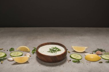 Tasty tzatziki sauce in wooden bowl with ingredients and spices on stone surface on black background clipart