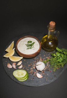 Ev yapımı tzatziki sosu. İçindekiler, baharatlar ve siyah zemin üzerinde zeytinyağı.