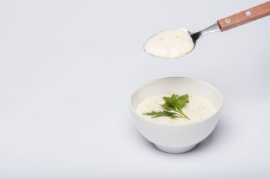 Tasty tzatziki sauce with greenery and spoon on white background clipart