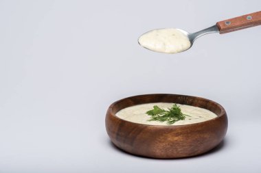 Tasty tzatziki sauce with greenery in wooden bowl and spoon on white background clipart
