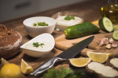 Lezzetli tzatziki sosunun seçici odak noktası. Mutfak masasında ham malzemeler var. 