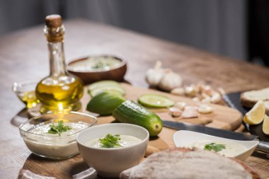 Delicious tzatziki sauce with ingredients and olive oil on wooden kitchen table  clipart