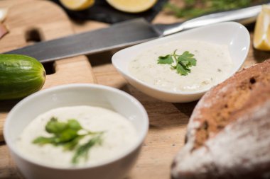 Tzatziki soslu, ahşap masadaki ekmekli kaselerin seçici odağı 