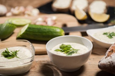 Selective focus of traditional greek tzatziki sauce with ingredients on wooden table  clipart