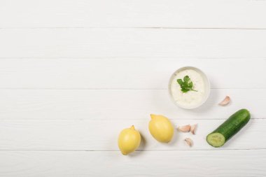 Beyaz ahşap zemin üzerinde limonlu, salatalıklı ve sarımsaklı tzatziki sosu.