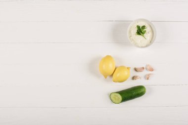 Beyaz ahşap arka planda ev yapımı tzatziki sosu, limon, salatalık ve sarımsak.
