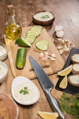 Tzatziki sosu, taze malzemeler ve ahşap masada ekmek.