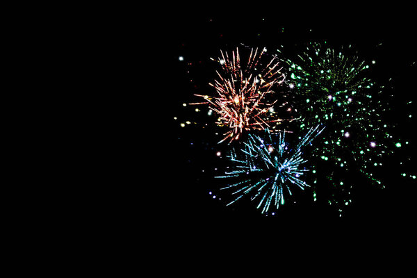 blue, green and orange traditional fireworks in dark night sky, isolated on black
