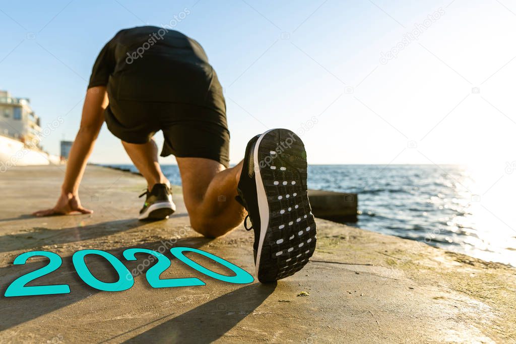 young runner standing in start position on embankment near 2020 lettering