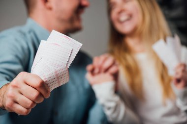 cropped view of happy man and woman holding hands while holding lottery tickets clipart