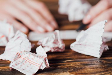 selective focus of crumpled lottery tickets near gambler marking numbers in lottery card on wooden table clipart