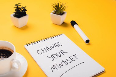 notebook with change your mindset inscription near coffee cup, potted plants and felt-tip pen on yellow desk clipart