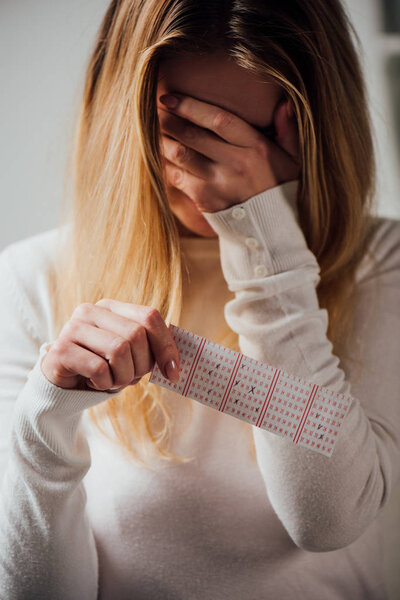 upset woman covering face with hand while holding lottery ticket