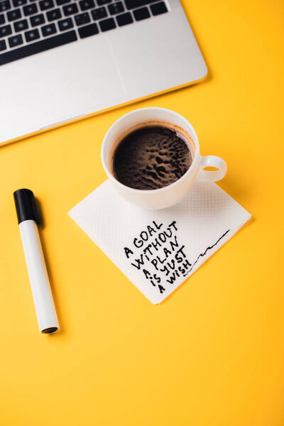 Кофейная чашка на бумажной салфетке с целью без плана просто желаем надпись, ноутбук и ручка на желтом столе
