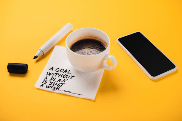 Кофейная чашка на бумажной салфетке с целью без плана просто желаем надпись, смартфон и наконечник ручки на желтом столе
