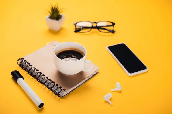 コーヒーカップ スマートフォン ワイヤレスイヤフォン 鉢植え 黄色い机の上のフェルトペン — ストック写真
