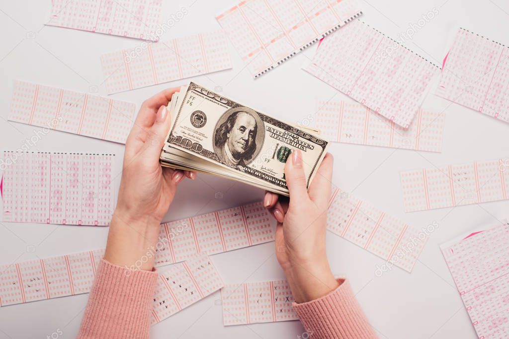 cropped view of woman holding dollar banknotes near scattered lottery tickets on white table