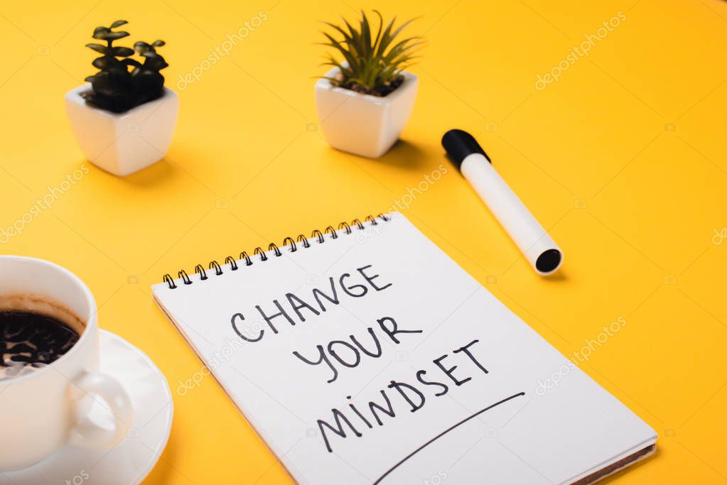 notebook with change your mindset inscription near coffee cup, potted plants and felt-tip pen on yellow desk