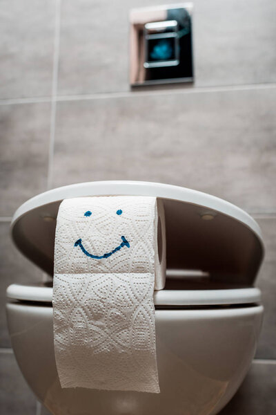 close up view of ceramic clean toilet bowl and toilet paper with smiley face in modern restroom 