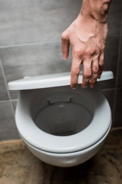 Modern tuvalette klozet kapağı tutan gri fayanslı adam manzarası.