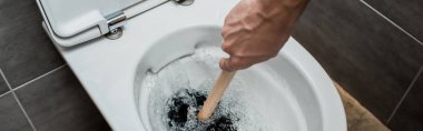 cropped view of plumber using plunger in toilet bowl during flushing in modern restroom with grey tile, panoramic shot clipart