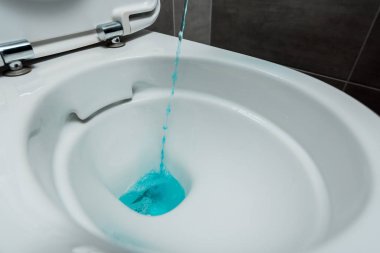 Modern tuvaletteki seramik temiz klozete gri fayansla dökülen mavi sıvı deterjan manzarasını kapatın.